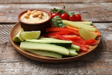 Tasty homemade hummus with chickpeas and different vegetables on wooden table