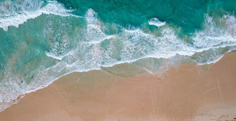 Fototapeta premium Aerial view of a sandy beach with turquoise waves crashing onto the shore scattered people are seen walking along the coastline