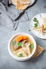 Traditional Jewish Kreplach soup with meat and carrot, gray background