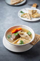 Traditional Jewish Kreplach soup with meat and carrot, gray background