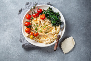 A delicious plate of creamy hummus garnished with fresh tomatoes, leafy greens, and served with pita bread