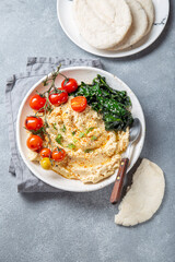 A delicious plate of creamy hummus garnished with fresh tomatoes, leafy greens, and served with pita bread