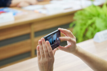 Video and photography using a smartphone of a meeting taking place in the office. A woman's hands hold a smartphone in camera mode. Report, podcast or video blogging. Photo. Selective focus.