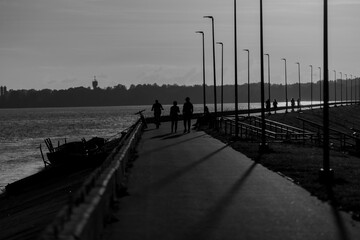 Black and white silhouette photo of people walking by the river