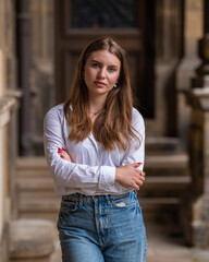 Close up portrait of a beautiful young Caucasian woman, cute girl on a city street, looking at the camera outdoors. She folded her hands on her chest. Lifestyle, female beauty concept.