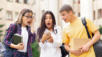 Shocked students checking exams results online on smartphone, resting in campus