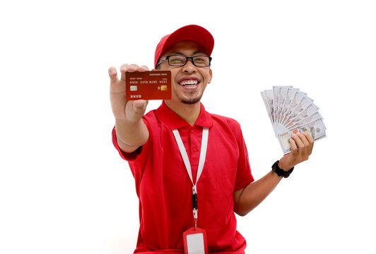Asian delivery man wearing a red polo shirt holds a credit card and dollar banknotes against a white background. Delivery services, financial transactions, e-commerce, and customer satisfaction.