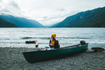 The woman is taking a break from canoeing on Lake Crescent and relaxing on the beach while drinking a cup of coffee. © Victoria Nefedova
