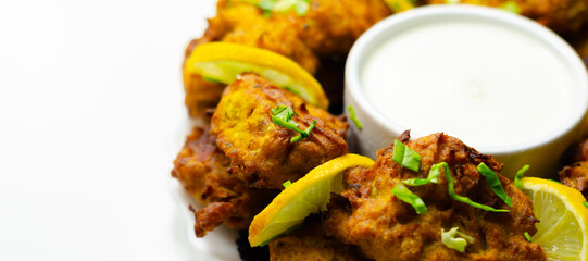 A plate of fried food with a white sauce and lemon wedges