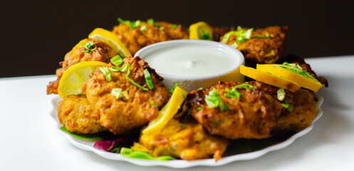 A plate of fried food with a white sauce and lemon wedges