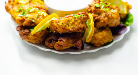 A plate of fried food with a white sauce and lemon wedges