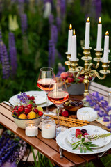 Beautiful romantic outdoor wedding decor in a field. Table decorated with purple lupines flowers. Wineglasses with white wine. Sunset, summer, golden hour. Perfect surprise date for loving couple