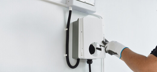 A man electrician installing a home charging, installing charging station for electric car at private house