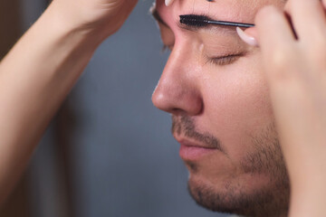 A man is having his eyebrows groomed by a professional beautician using tweezers