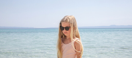 Portrait of 7 years old girl in pink swimsuit and long blonde hair with blue sea and sky in the background