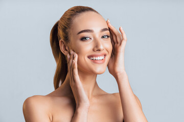 A young woman with long brown hair tied back in a ponytail smiles brightly at the camera. She is...
