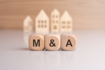 letters M and A on wooden blocks and house models on background, concept for Mergers and Acquisitions