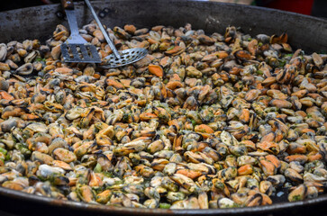 Large pan filled with an array of grill frying mussels at street food festival, ready to eat