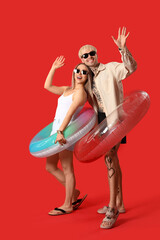 Young couple with inflatable rings waving hands on red background