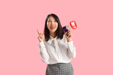 Naklejka premium Beautiful Asian woman with funny megaphone pointing at something on pink background. Dialogue concept