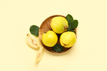 Wooden plate with sweet ripe quinces and leaves on yellow background