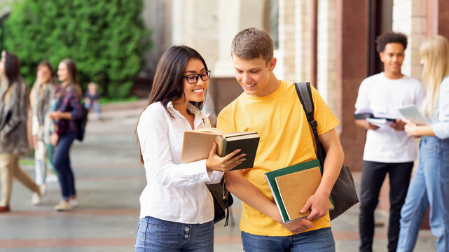 Student couple going to college class, reading book outdoors in university campus