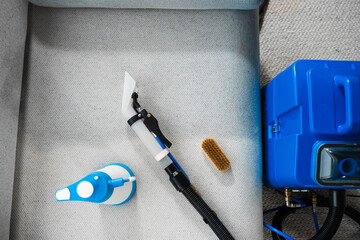 Cleaning equipment to dry cleaning gray sofa at home. Using extractor, spray detergent and brush to...