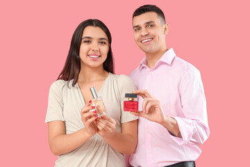 Young couple with bottles of perfume on pink background