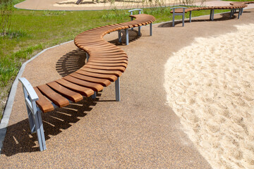 Modern curved wooden bench without backrest on playground