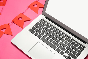 Laptop with paper garland on pink background. Concept of online dating