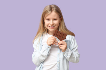 Happy little girl with sweet chocolate bar on lilac background