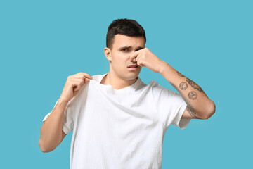 Handsome young man feeling bad smell from dirty clothes on blue background