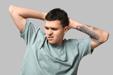 Handsome young man feeling bad smell from armpits on grey background
