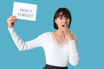 Surprised young woman holding paper sheet with text DON'T FORGET on blue background