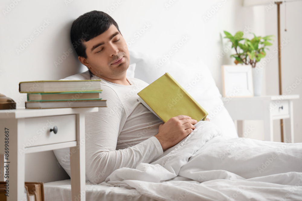 Wall mural Young man with book sleeping in bedroom