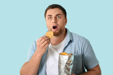 Handsome young shocked man with tasty potato chips on blue background