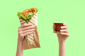 Hands with tasty doner kebab and drink on green background