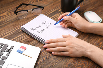 Woman writing in French on wooden table, closeup