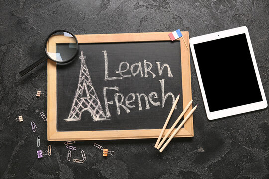 Chalkboard with text LEARN FRENCH, stationery and tablet computer on dark background