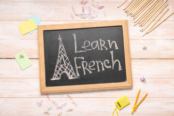 Chalkboard with text LEARN FRENCH and different stationery on light wooden background