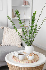 Cup of tea and vase with tree branches on coffee table in living room