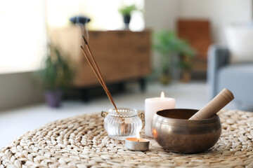 Tibetan singing bowl with aroma sticks and burning candles on pouf in living room, closeup