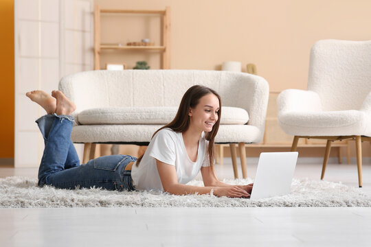 Young happy woman lying on floor and using laptop near sofa in living room