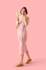 Young woman with mini green electric fan using mobile phone on pink background
