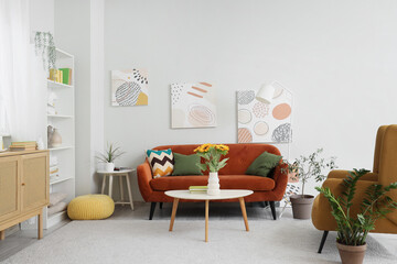 Fototapeta premium Comfortable sofa and sunflower in vase on table in living room