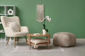 Armchair with pillow, pouf and coffee table with orchid in living room