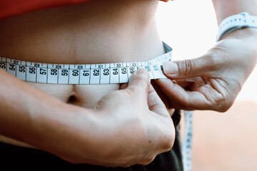 A woman takes her waist measurements with a measuring tape. According to the World Health...