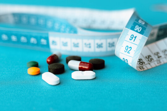 Antibiotic tablets (amoxicillin and norfloxacin), activated charcoal and flu medicine are seen next to a measuring tape. Some medications can cause side effects that, over time, can cause weight gain.