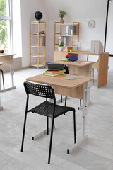 Interior of light classroom with desks, teacher's table and shelf units