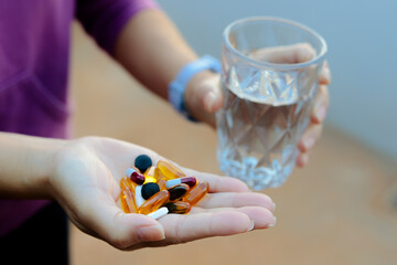 In this photo illustration, several medicine pills in a person's hand and holding a glass of water.